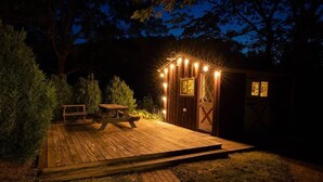 Een houten terras met een picknicktafel en een kleine schuur, verlicht met lichtslingers.