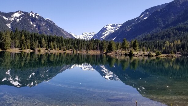 A clear lake reflecting mountains and dense forest.