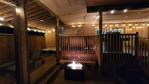 A cozy wooden interior with a fire feature, seating, and string lights.