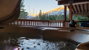 A hot tub with a wooden deck and a view of snow-capped mountains.