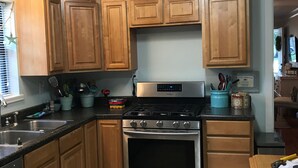 A kitchen with wooden cabinets, a stainless steel stove, and a tiled floor. - Hayden Cottage. Great location and comfortable cottage. (Pass Christian)