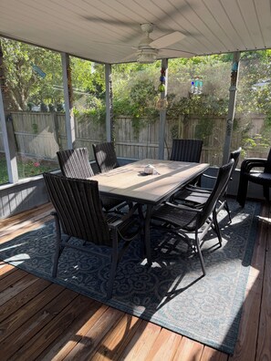 Eine überdachte Terrasse mit Tisch und Stühlen, einem Deckenventilator und Blick auf den Garten.