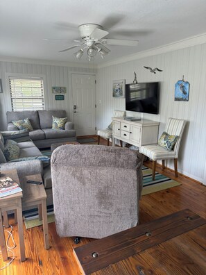 A living room with a grey sofa, a white cabinet, a television, and a ceiling fan.