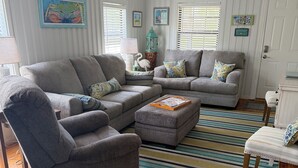 A living room with a grey sofa set, a wooden floor, and a striped rug. - Hayden Cottage. Great location and comfortable cottage. (Pass Christian)