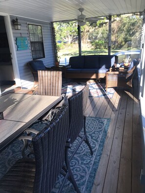 Eine überdachte Terrasse im Freien mit Korbmöbeln, einem Tisch und einem Deckenventilator.
