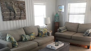 A living room with two sofas, patterned cushions, a coffee table, and a decorative wall piece. - Hayden Cottage. Great location and comfortable cottage. (Pass Christian)
