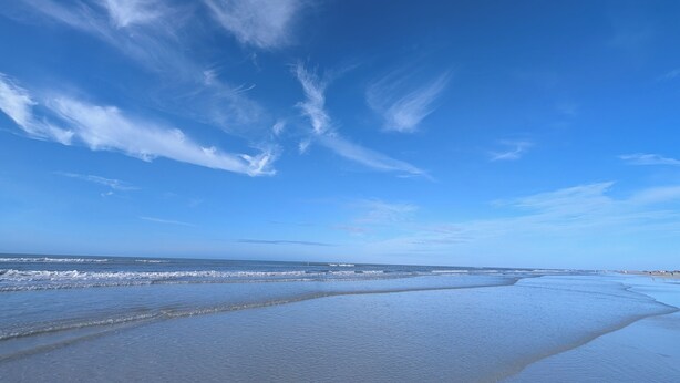 Una playa con cielos despejados y olas suaves.
