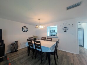 Un coin repas comprenant une table, des chaises, une horloge et une fenêtre donnant sur la cuisine.