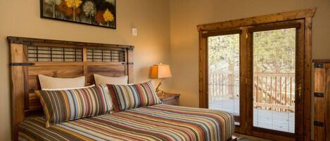 A bedroom with a wooden headboard, a bed with striped bedding, a nightstand with a lamp, and a window with blinds.