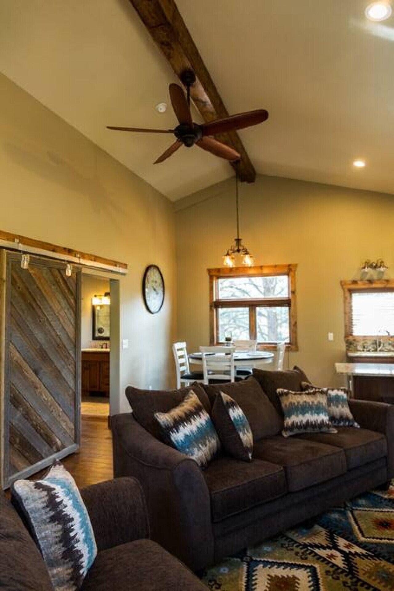 A cozy living room with a brown sofa set, a ceiling fan, and a dining area with a table and chairs.