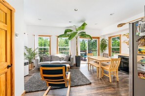A bright, open-plan living and dining area with a large window, a sofa, a dining table, and chairs. - Modern Cabin on a River Bluff (Mason)