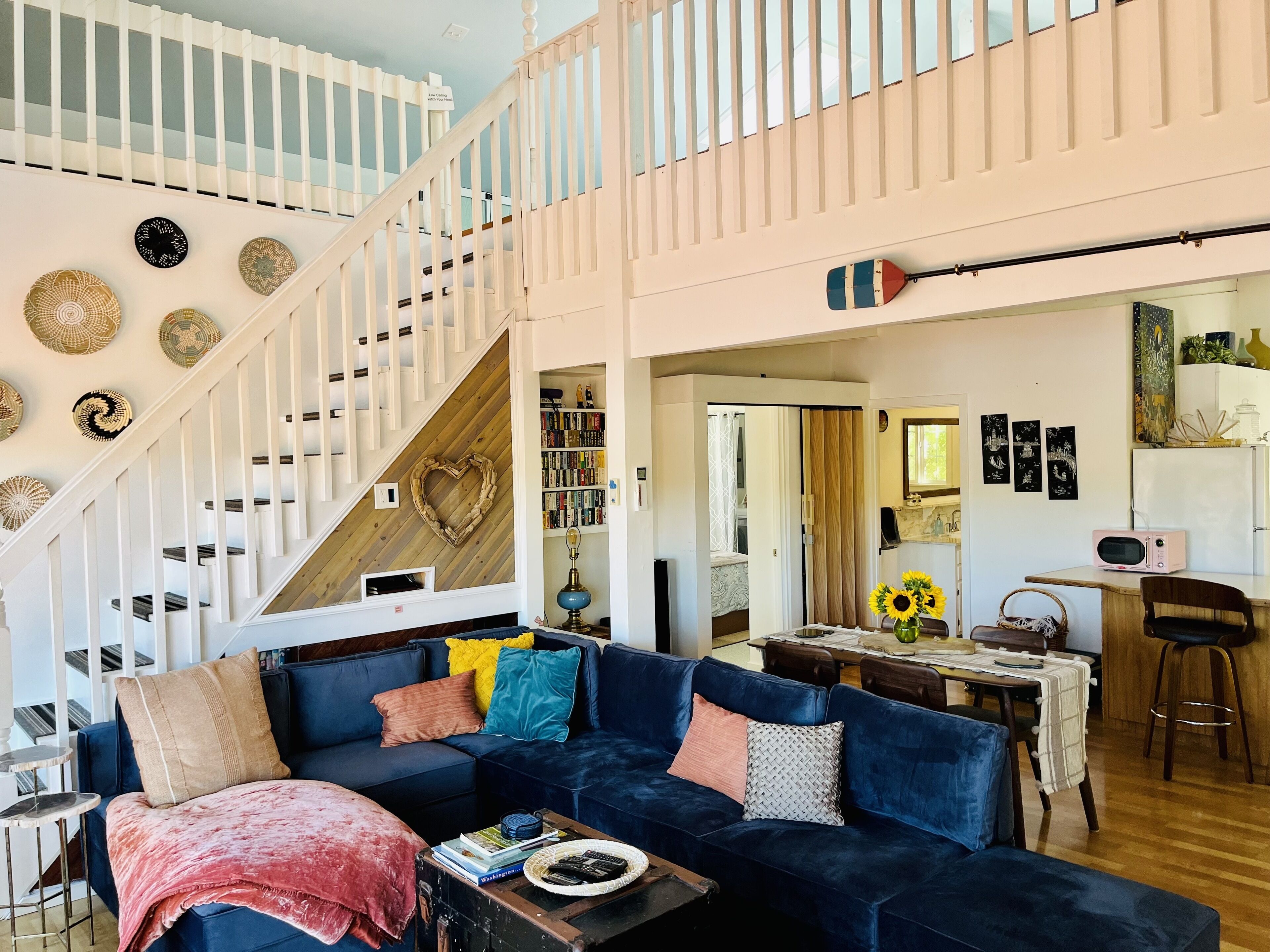 Un vaste espace de vie comprenant un canapé bleu, un escalier en bois et un coin repas avec une table et des chaises.