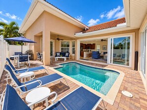 A pool area with lounge chairs, a barbecue, and a covered patio.
