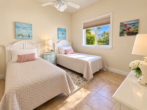 A bedroom with two beds, a ceiling fan, artwork on the walls, and a window with a view of greenery. -  Best Value In Naples Grand luxury 3 Bdrm Pool Spa Walk Bike To Gulf Spotless (Naples)