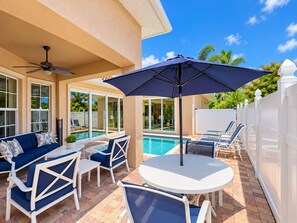 A poolside area with a white fence, a blue sofa, and a table with chairs. -  Best Value In Naples Grand luxury 3 Bdrm Pool Spa Walk Bike To Gulf Spotless (Naples)