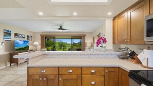 A kitchen with wooden cabinets, a granite countertop, a ceiling fan, and a view of greenery outside. - ~ The Kauai Luna ~ Ocean - Waterfall & Sunset View (Princeville)