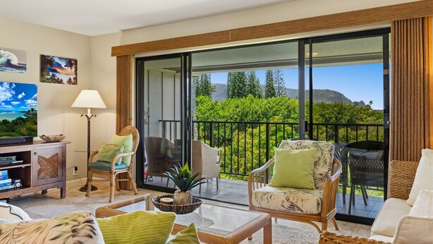 A spacious living room with a balcony, a ceiling fan, and a television. - ~ The Kauai Luna ~ Ocean - Waterfall & Sunset View (Princeville)