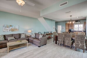 A spacious living room with a sectional sofa, a coffee table, and a dining area with wicker chairs.