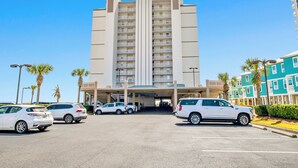 A multi-story hotel with a central entrance, parking lot, and adjacent colorful buildings.