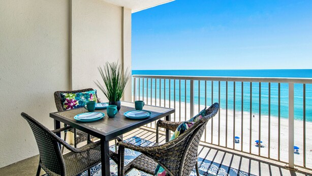 A balcony with a table set for two, overlooking a beach.