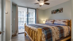 Une chambre avec un lit en bois, un ventilateur de plafond et une grande fenêtre avec des rideaux.