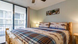 Une chambre dotée d’un grand lit, d’un ventilateur de plafond, d’une fenêtre donnant sur un balcon et d’une œuvre d’art accrochée au mur.