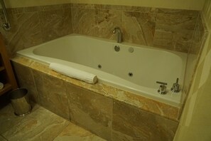 A bathroom with a marble bathtub, a towel, and a metal trash can.