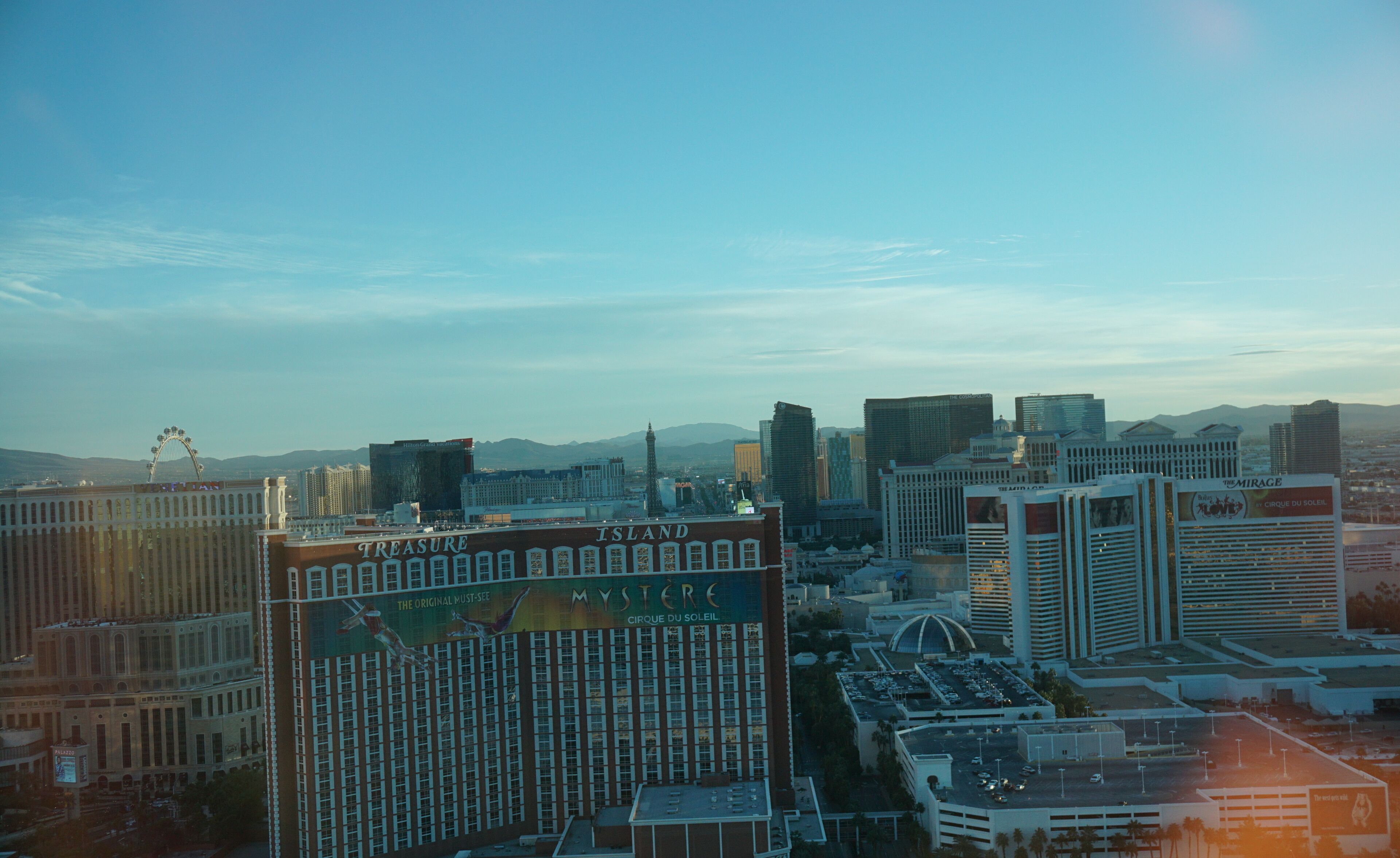 A cityscape with prominent buildings including a large hotel with a sign reading "Treasure Island" and "Mystère".