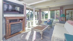 A living room with a fireplace, a television, a sofa, and a window with a view of greenery.