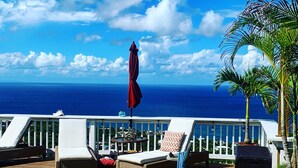 Un espace aménagé au bord de la piscine, avec des chaises longues, un parasol rouge et une vue sur l’océan.