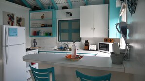 Une cuisine compacte dotée d’un îlot central, de meubles blancs et de touches de couleur turquoise.
