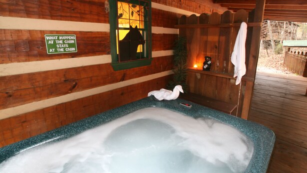 A wooden cabin interior with a hot tub, a sign reading "What happens at the cabin stays at the cabin," and a window with a silhouette of a horse. - Real Log Cabin. Pet Friendly, fenced yard! Only 5 Min to Pigeon Forge (Sevierville)