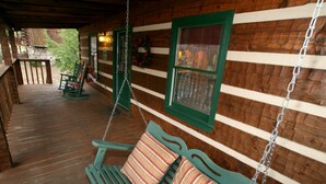 A wooden porch with a swing chair and a bench, a wooden fence, and a window with blinds. - Real Log Cabin. Pet Friendly, fenced yard! Only 5 Min to Pigeon Forge (Sevierville)