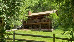 A two-story wooden cabin with a balcony, surrounded by lush greenery. - Real Log Cabin. Pet Friendly, fenced yard! Only 5 Min to Pigeon Forge (Sevierville)