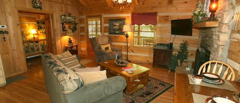 A cozy log cabin interior with a sofa, dining table, and fireplace.
