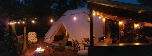 A tent with a fire pit, outdoor seating, and string lights.
