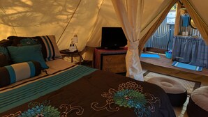 Un alojamiento en tienda de campaña acogedor, con cama, escritorio con lámpara y vistas al exterior.
