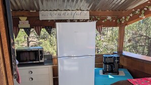 Cocina compacta con refrigerador, microondas y cafetera, debajo de una estructura de madera con vista a árboles.