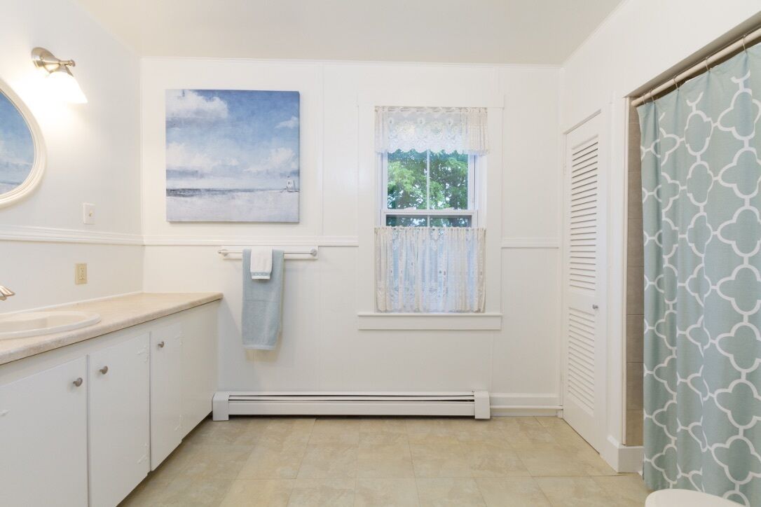 A bathroom with a window, a towel hanging on the wall, a heater, and a shower curtain.