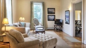 A living room with a sofa, armchair, and ottoman, a television, and framed pictures on the wall.
