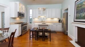 A modern kitchen with white cabinets, a stainless steel refrigerator, and a dining area with a glass table and wooden chairs.