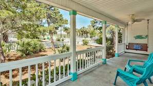 A covered porch with white railings and turquoise chairs, overlooking a landscaped area with trees and a white fence.