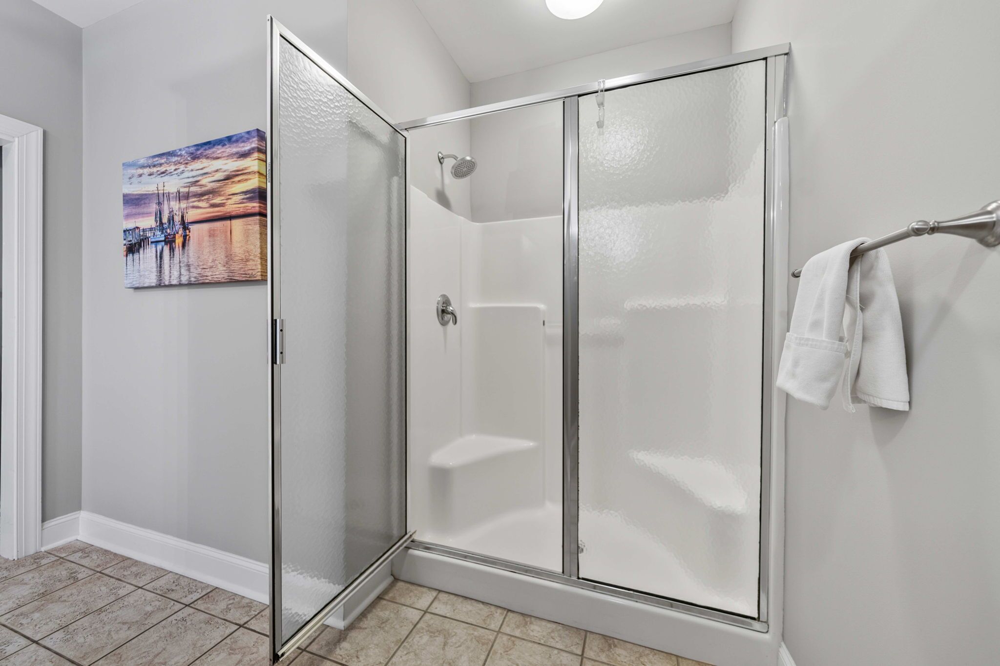 Eine gläserne Dusche mit weißem Handtuchhalter und einem Bild an der Wand.