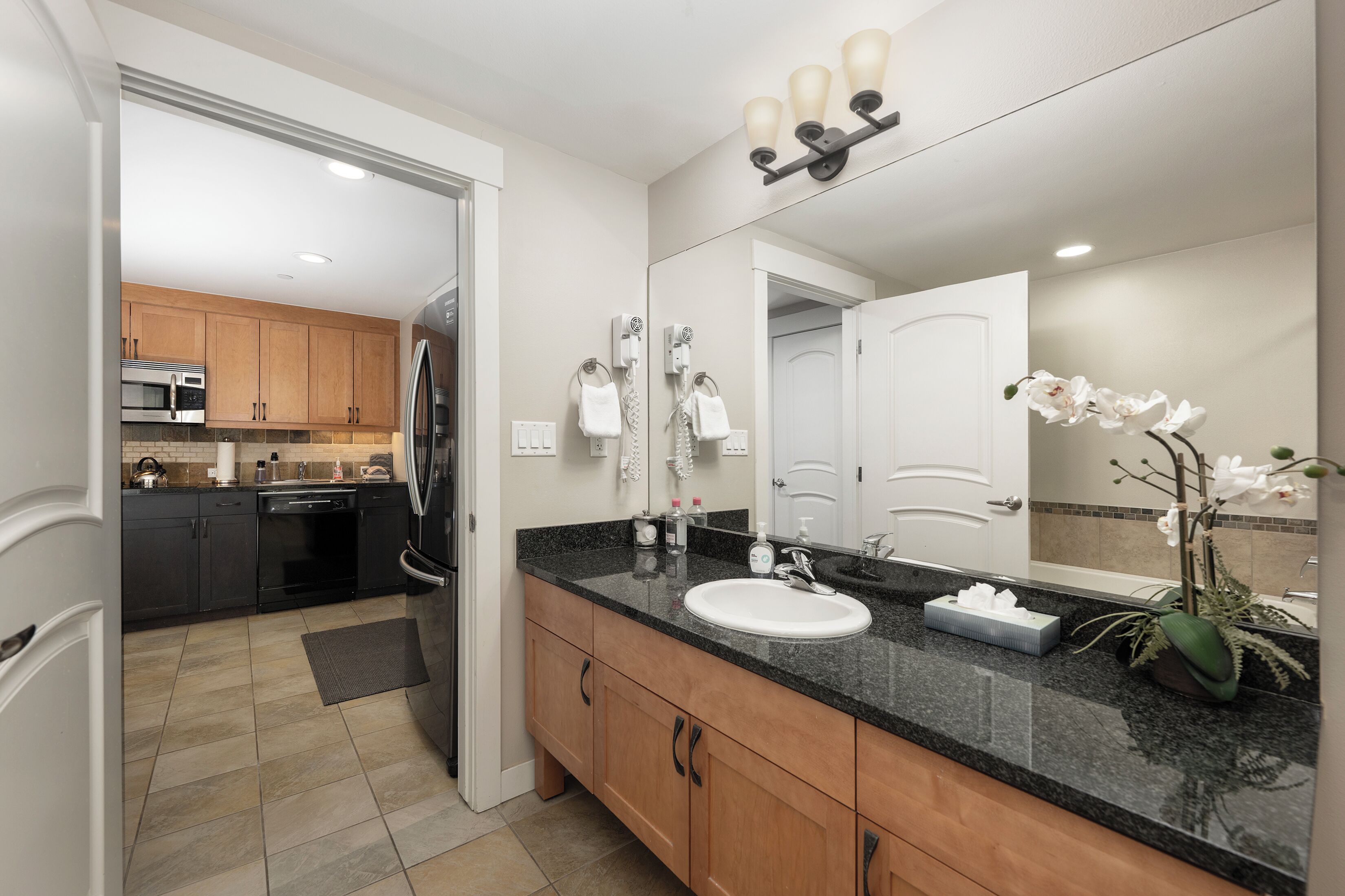 A modern bathroom with a large mirror, a sink, and a vanity. There is a shower area visible in the background.