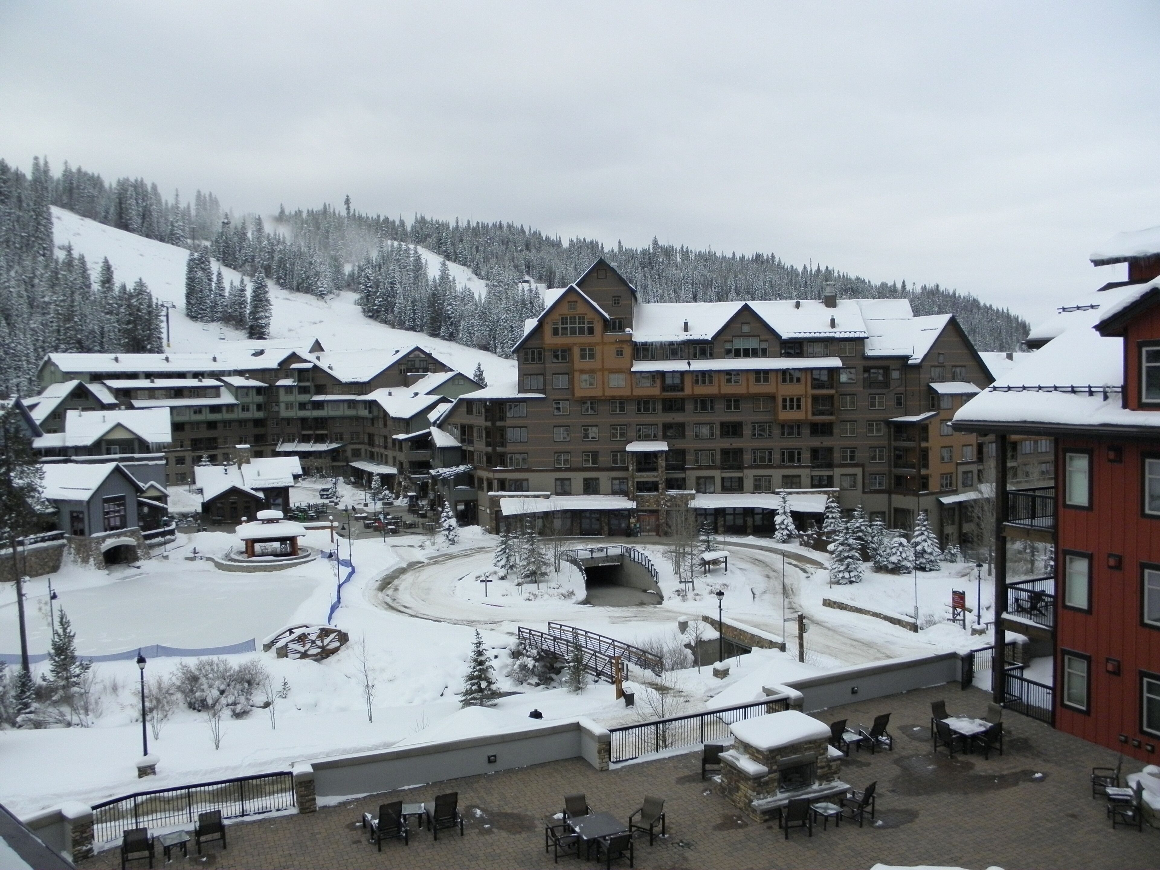 Ein schneebedecktes Resort mit mehreren Gebäuden, Außenbereichen zum Verweilen und einem zentralen Innenhof.