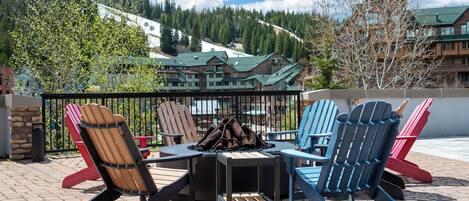 Une terrasse avec des fauteuils Adirondack et un foyer, offrant une vue sur un chalet de montagne.