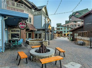Une rue pavée avec des tables en terrasse et un foyer central.