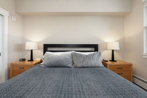 Un lit bien fait, recouvert d’une couvre-lit à motifs, avec deux lampes de chevet et une table de chevet sur laquelle se trouve une télécommande.