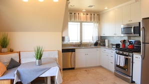 A modern kitchen with white cabinets, stainless steel appliances, and a dining area with a table and chairs. - San Diego Country Barndominium, Mountain Views, Spa, Deck, & More. (Valley Center)