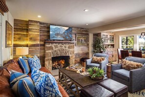 A cozy living room with a stone fireplace, comfortable seating, and a television mounted above it.
